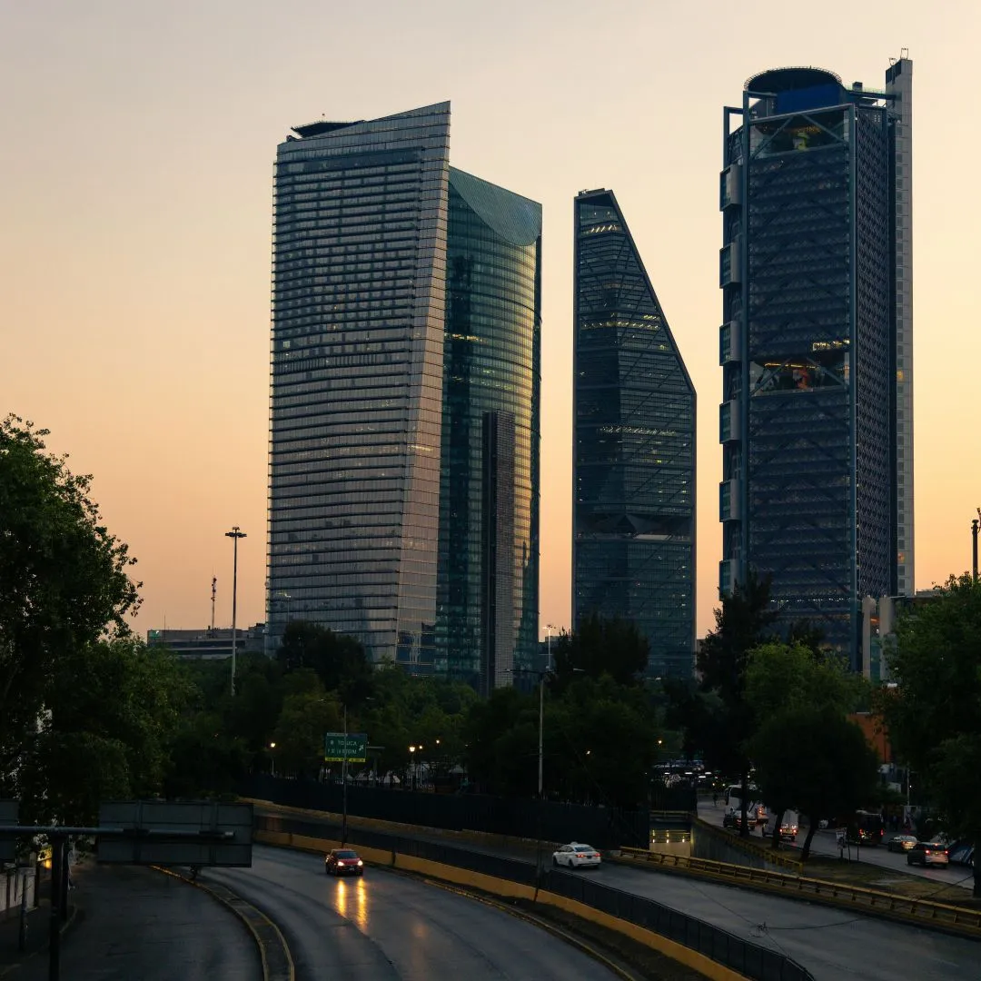 Cityscape with modern glass skyscrapers and a curved road with cars at sunset.