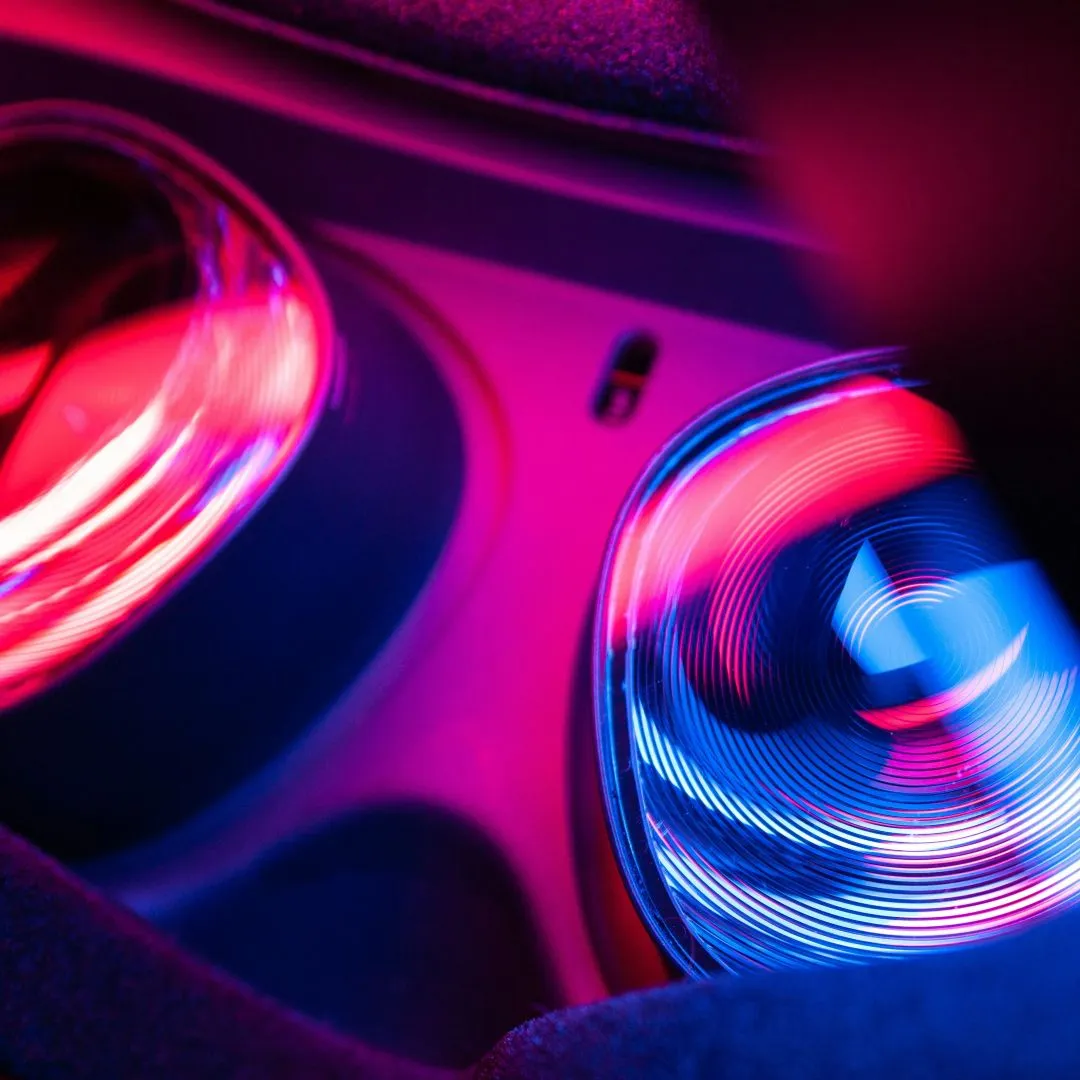 Close-up of a car's gear shift area with vibrant pink, red, and blue lighting reflections.