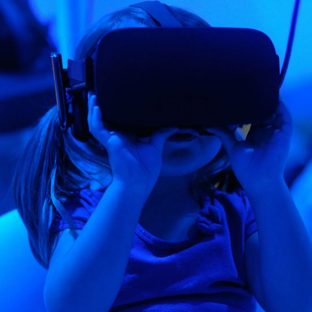 Young child wearing a virtual reality headset and touching it with both hands in blue light.