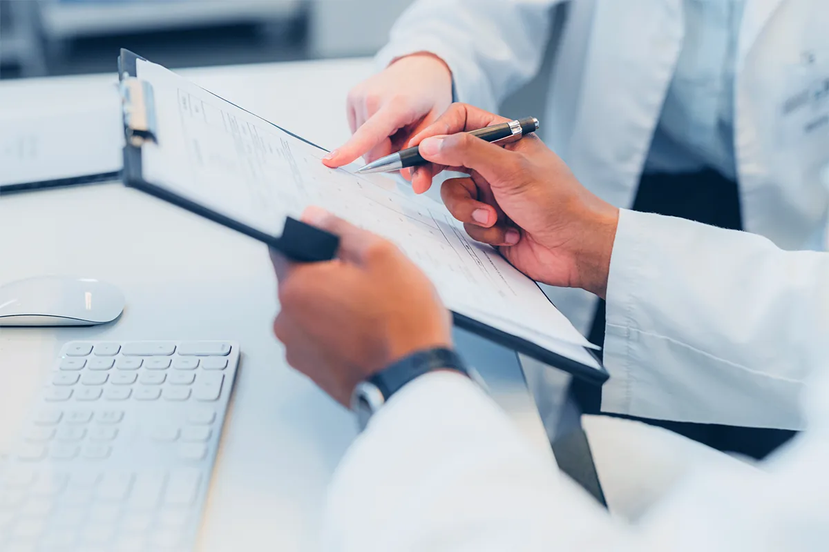 Clinician in a white coat reviewing a document on a clipboard