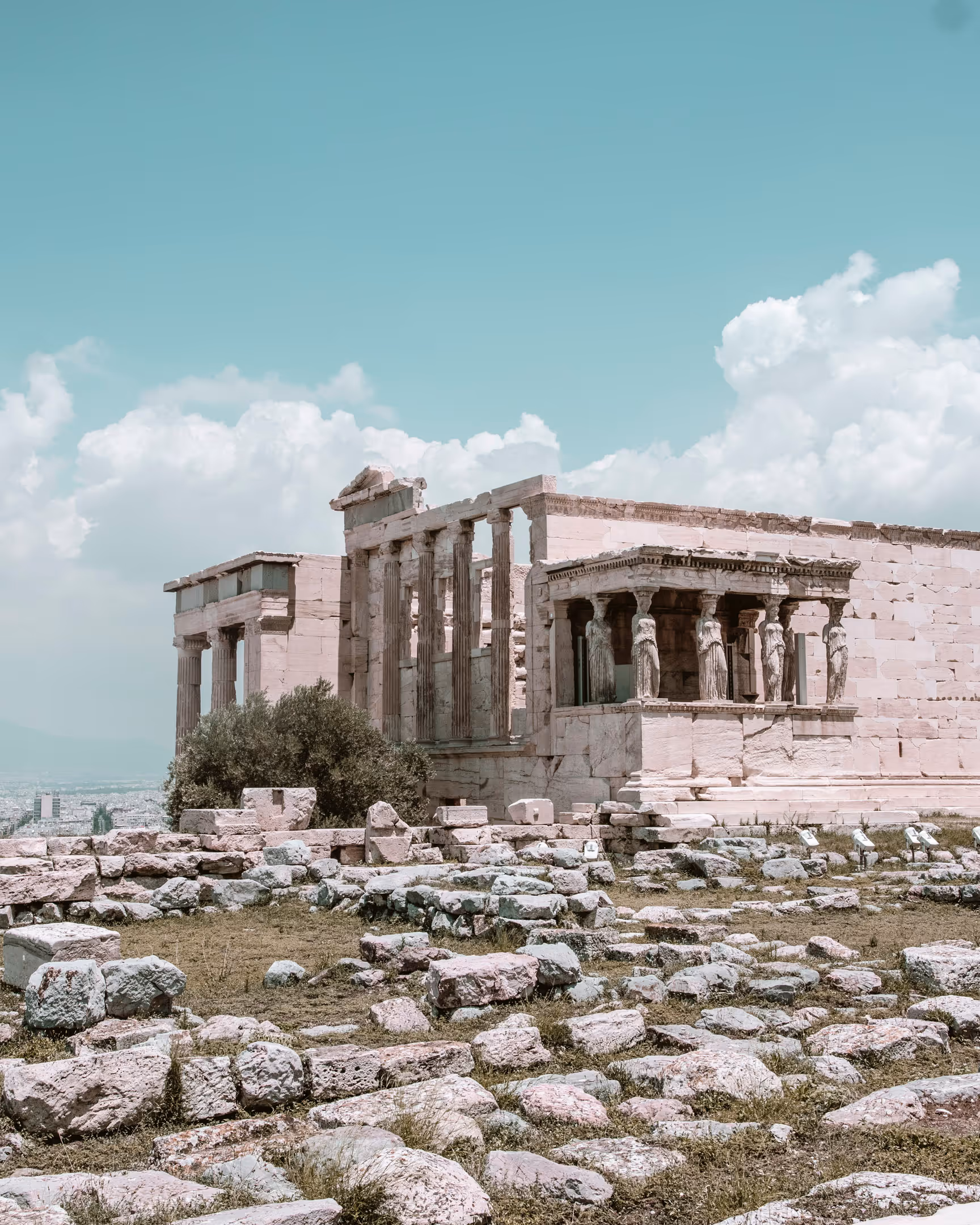 Ancient Greek temple ruins with columns and caryatid statues under a blue sky with clouds.