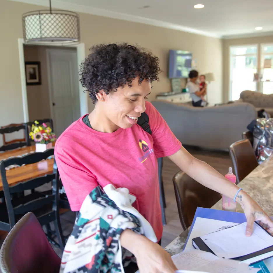 A cheerful young woman in a pink shirt organizing papers at home.