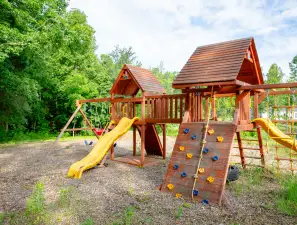 A wooden playground set featuring slides and climbing walls in a lush green environment.