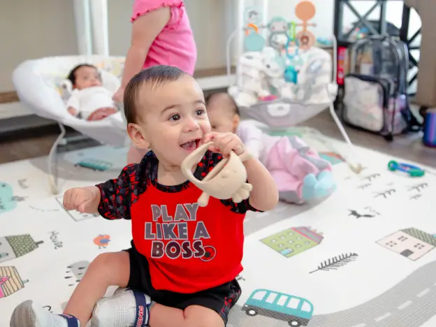 A happy baby wearing a red shirt playing with a teething toy on a colorful play mat.
