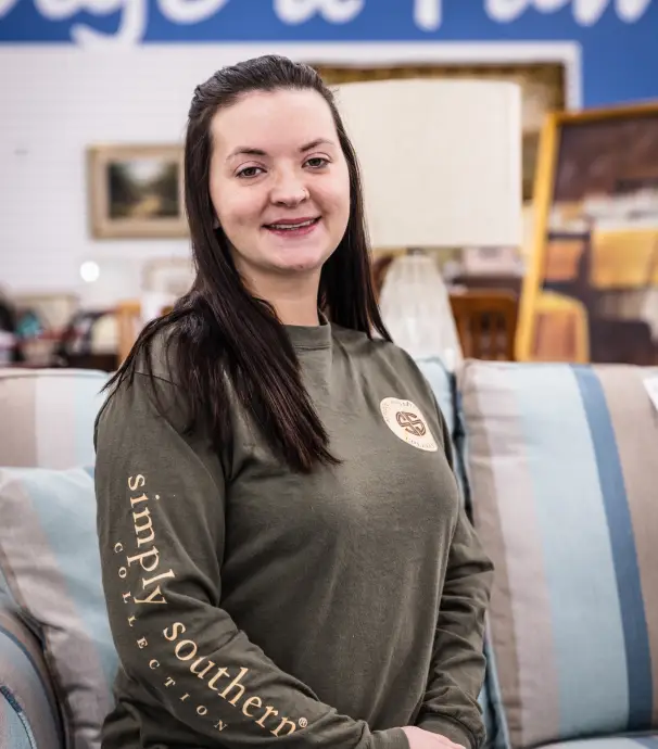 A smiling young woman posing in a thrift store, showcasing a stylish living space.