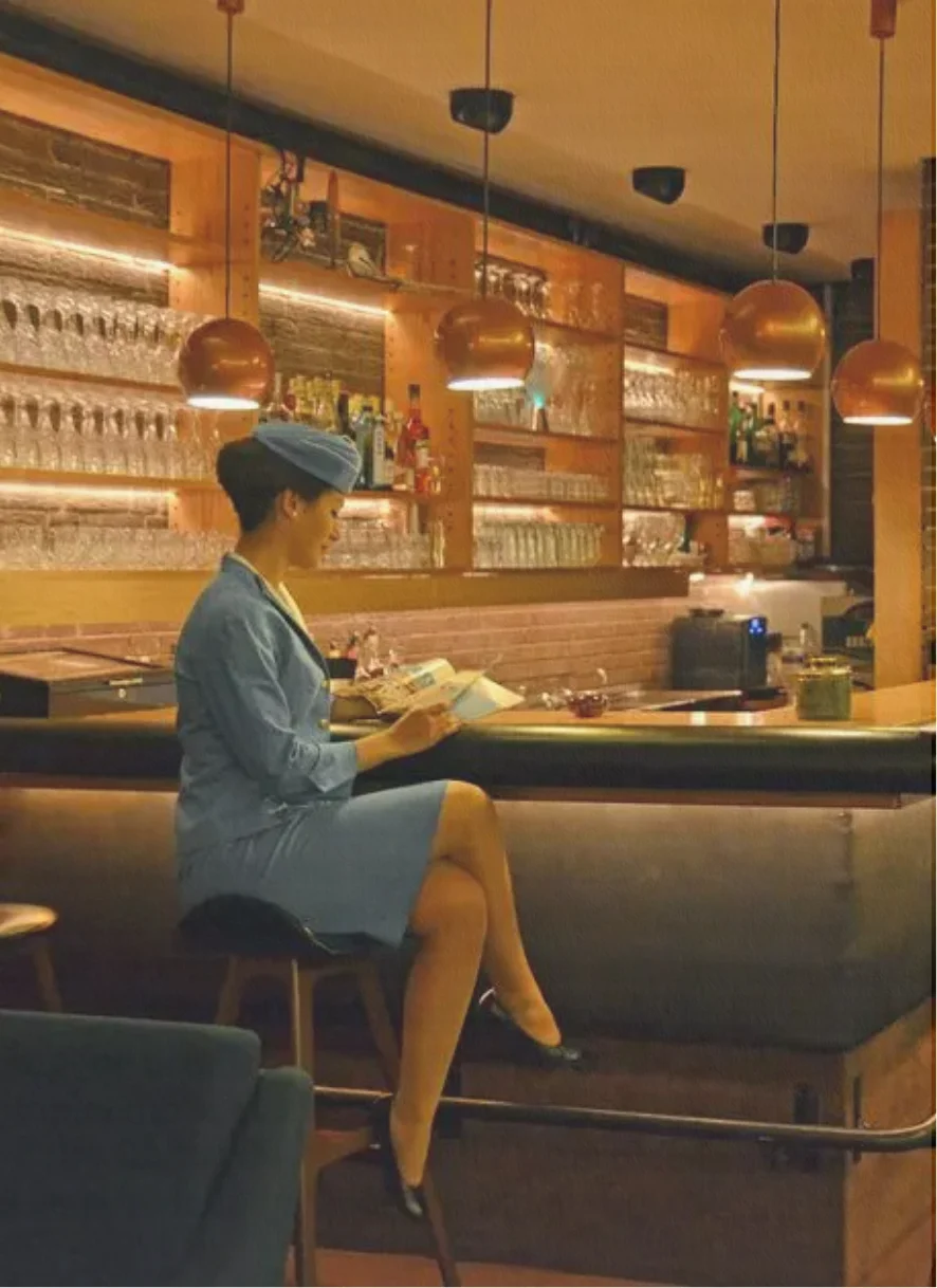 Warm terminal lounge with bar and ambient lighting, flight attendant sipping on a drink at the bar.