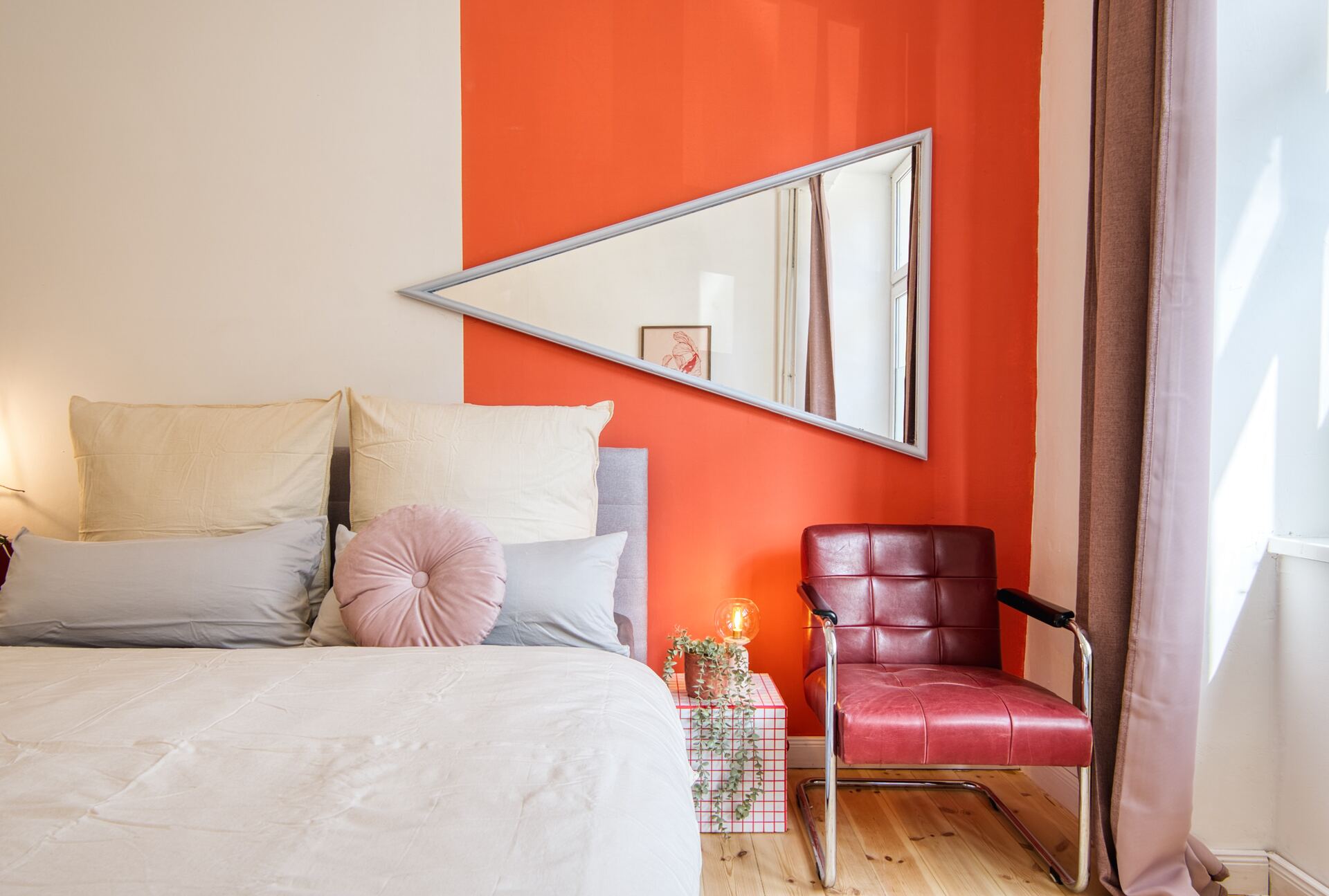 Bett mit roter Wand und künstlerischer Einrichtung, dreieckiger Spiegel
