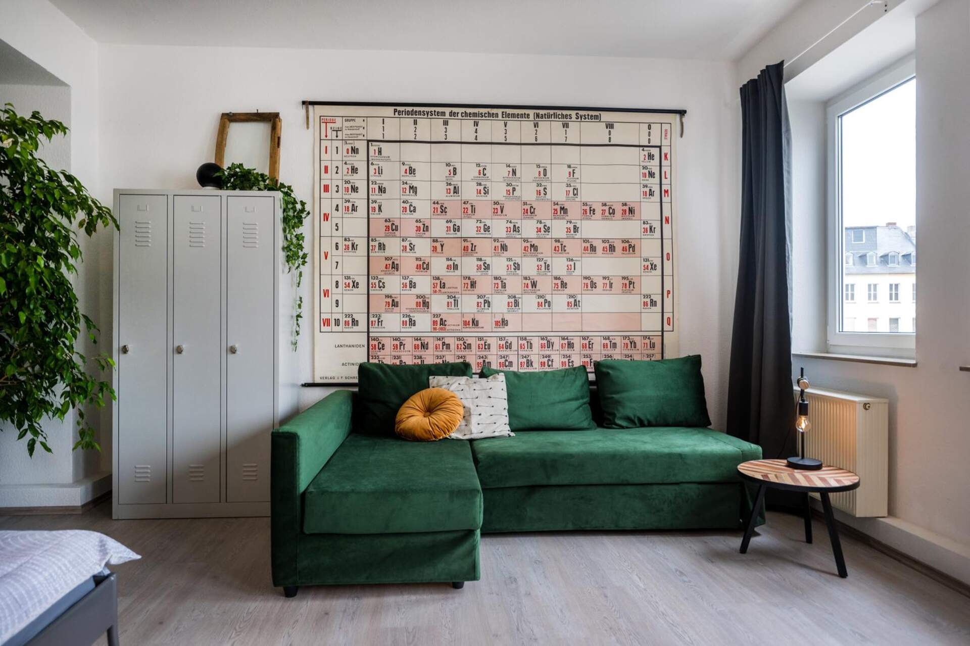 Grünes Samtsofa vor Vintage Plakat und grauem Metallspint im industrial Style