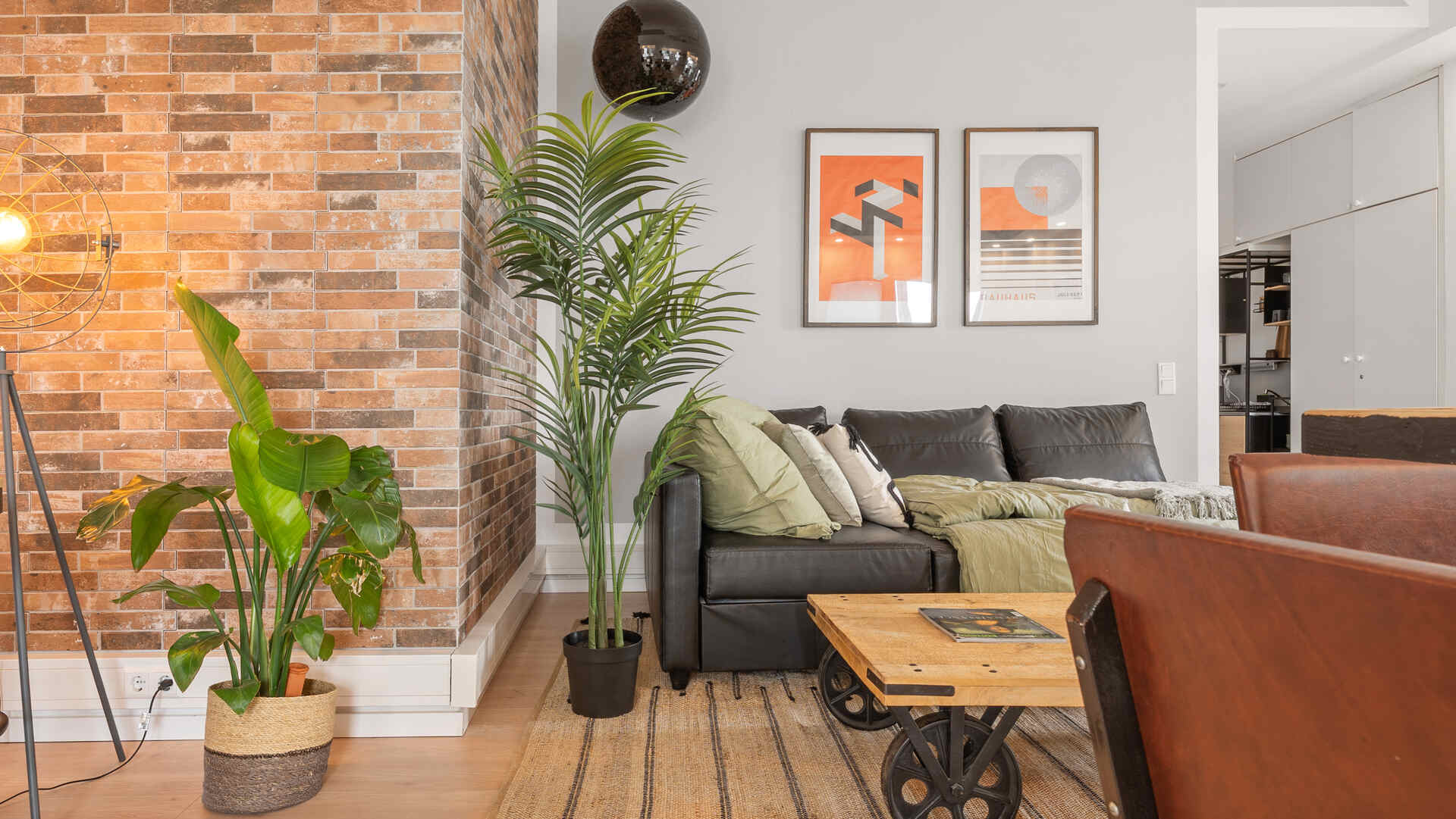 Wohnzimmer Ledercouch und schwarze Discokugel Klinkersteinwand und Pflanze Industrial Vibe