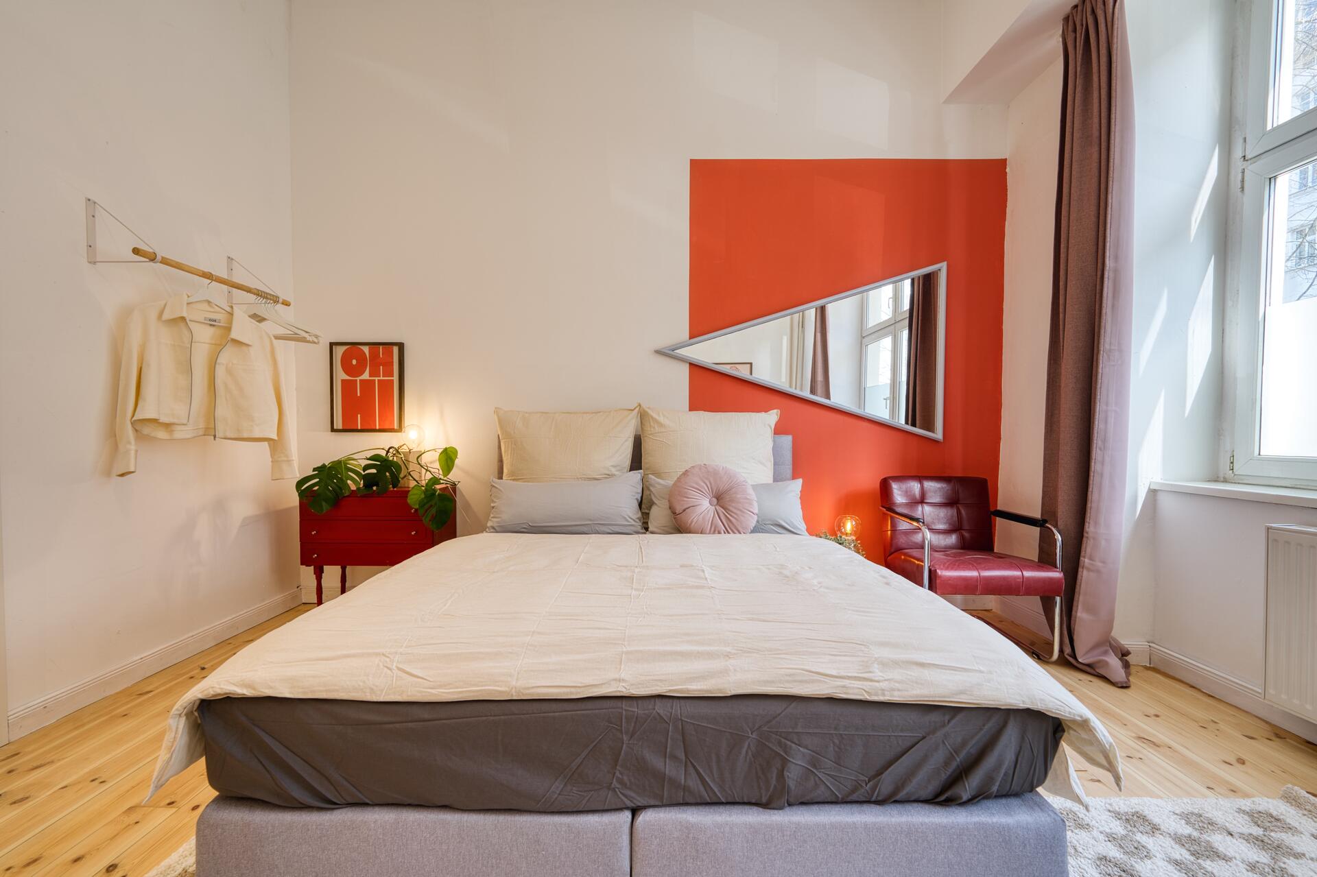 Schlafzimmer mit roter Akzentwand und dreieckigem Spiegel