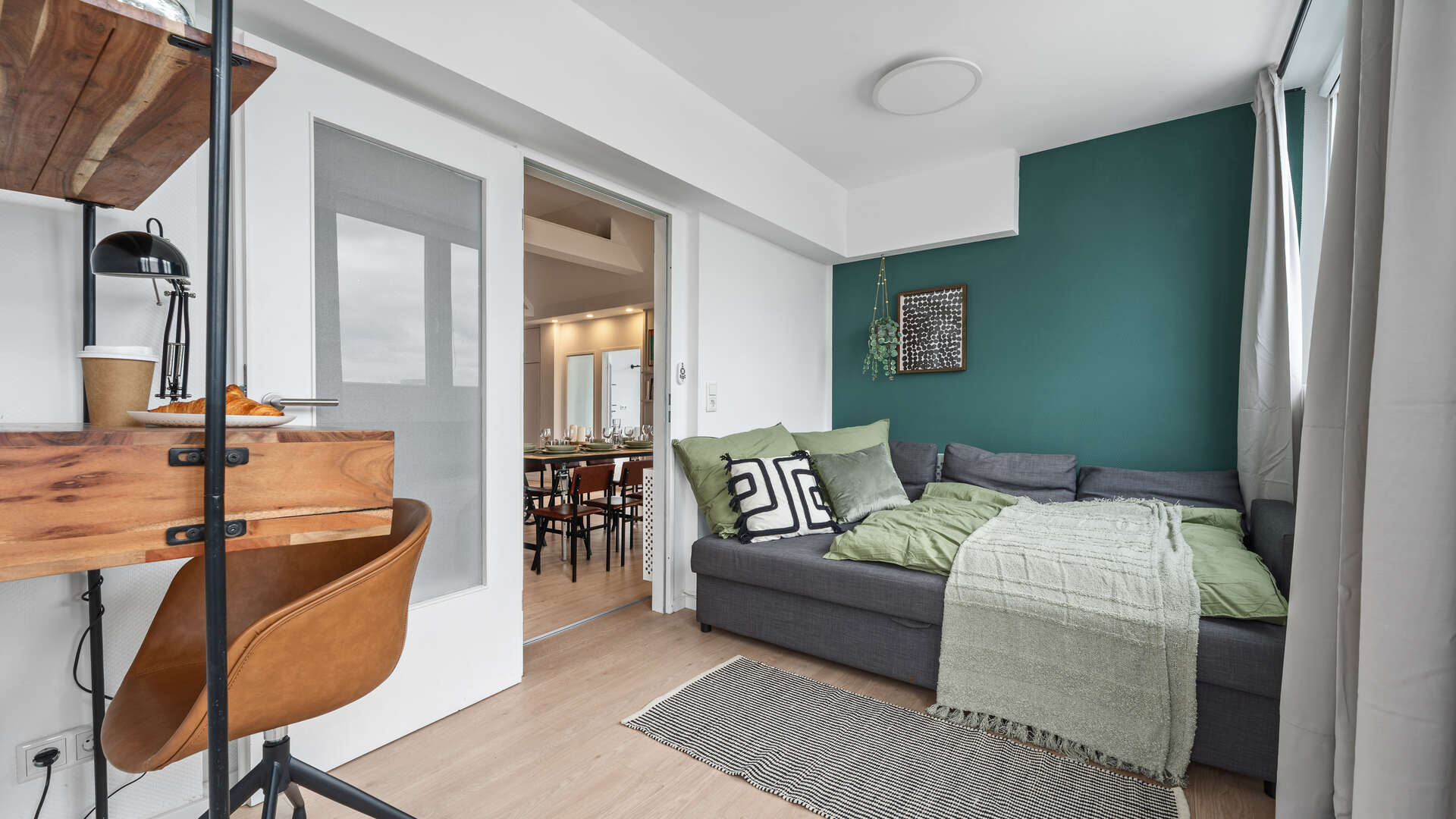 Schlafzimmer mit Schlafsofa und gruenen Akzenten und Schreibtisch in Arbeitsecke