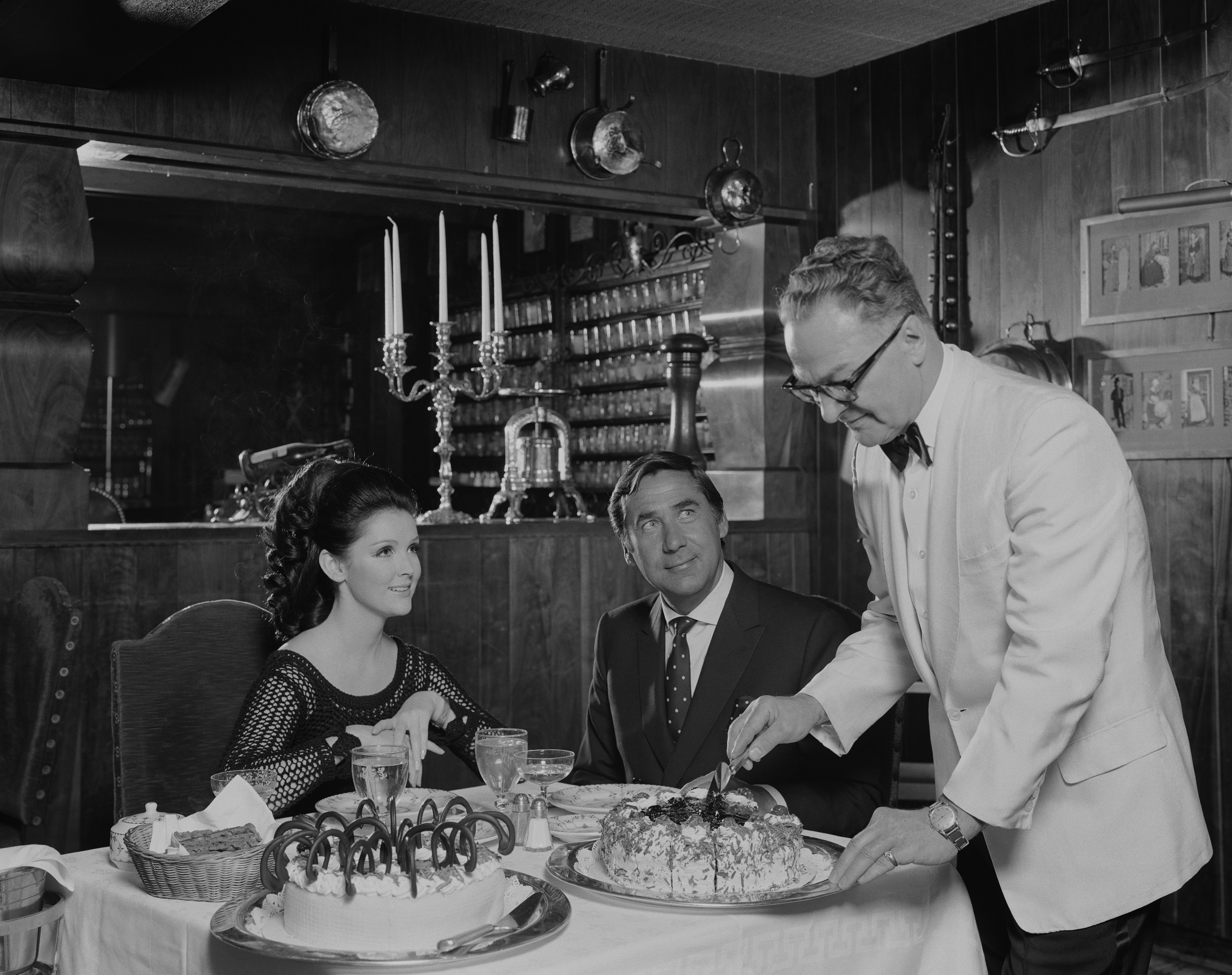 Suited waiter serving an elegantly dressed couple in a vintage black-and-white dining setting — Solara Society Dining & Events