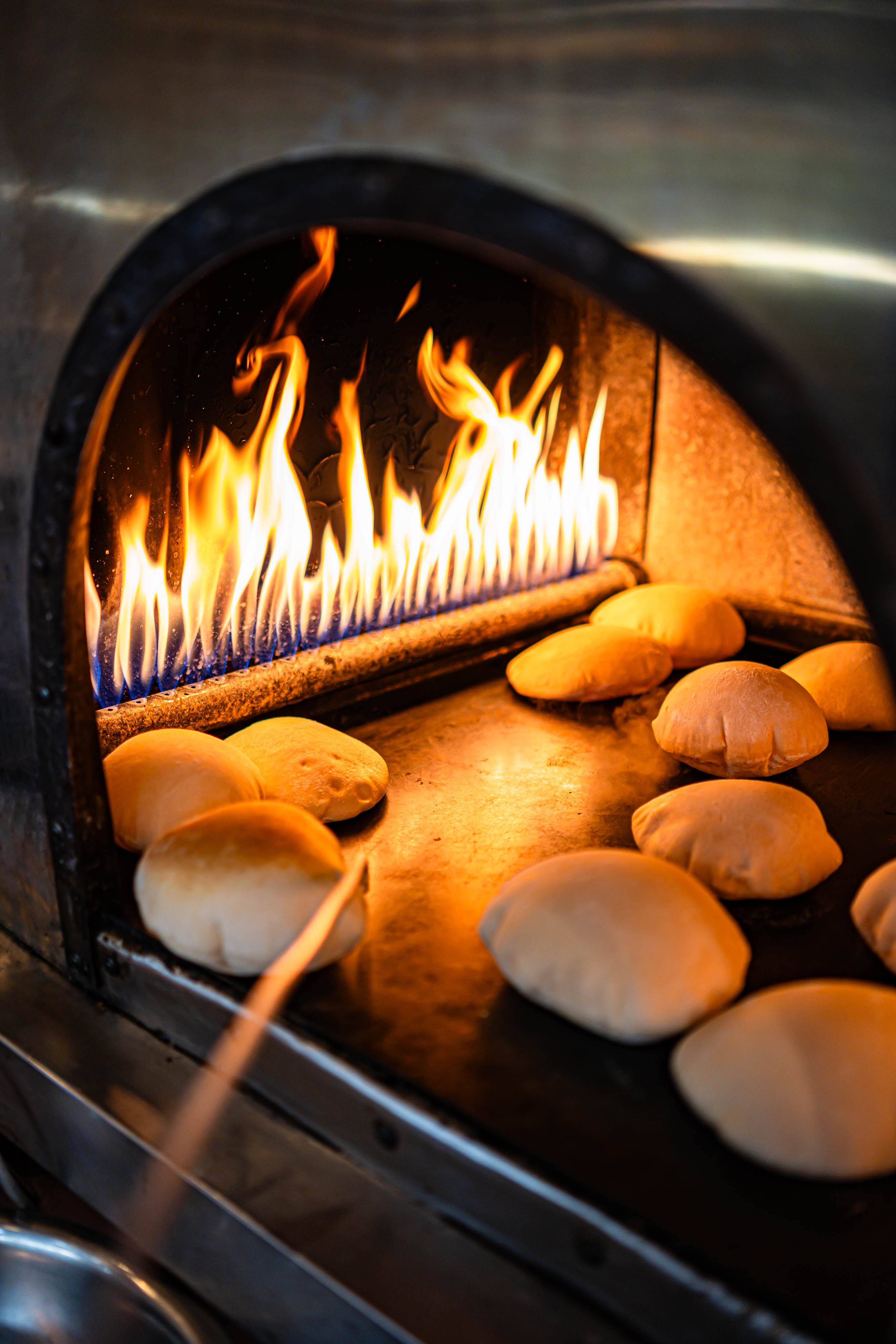 Pita bread baking inside a wood-fired oven with visible flames.