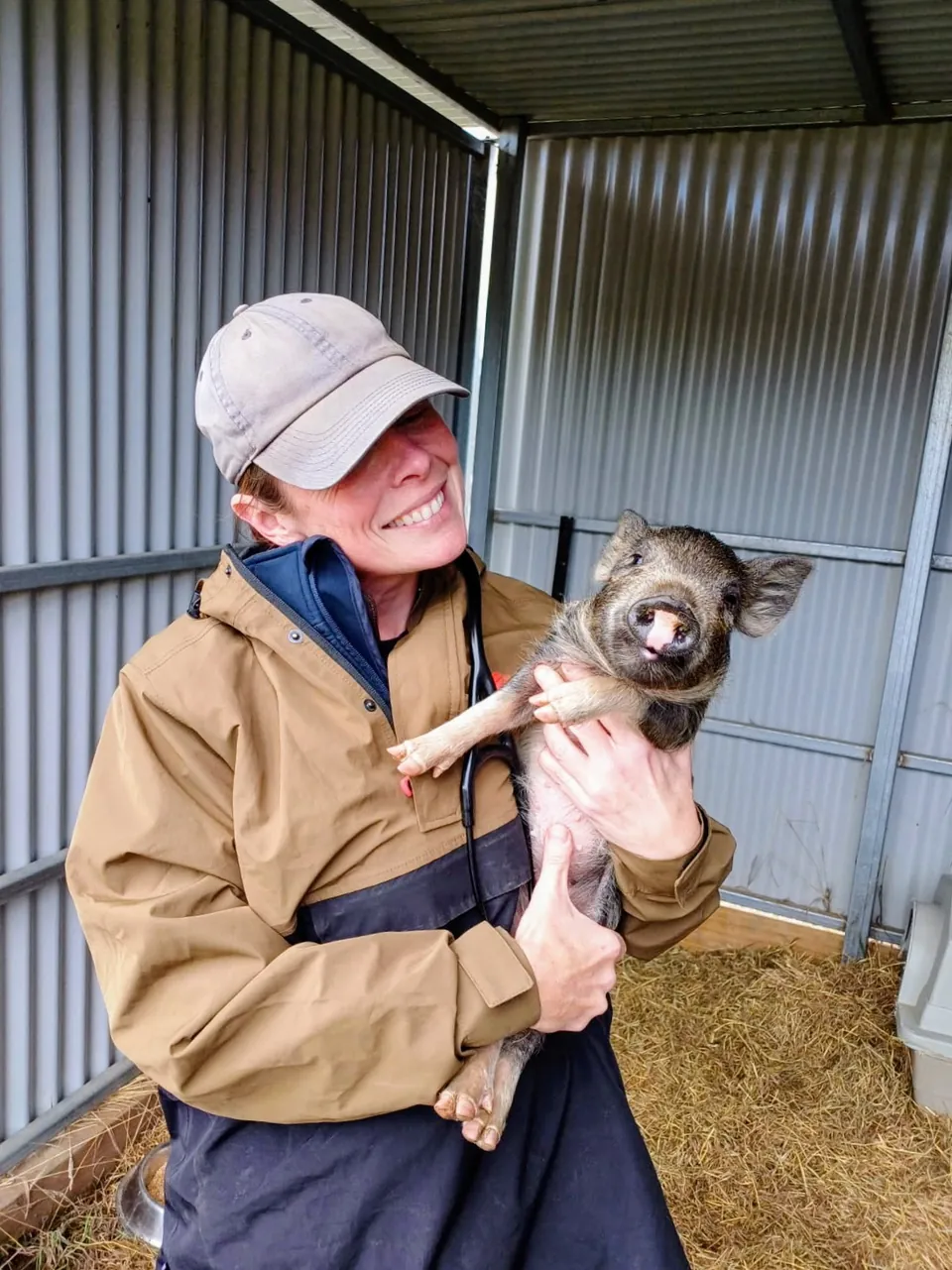 Adventure Vets team member cuddling a piglet in a farm shed