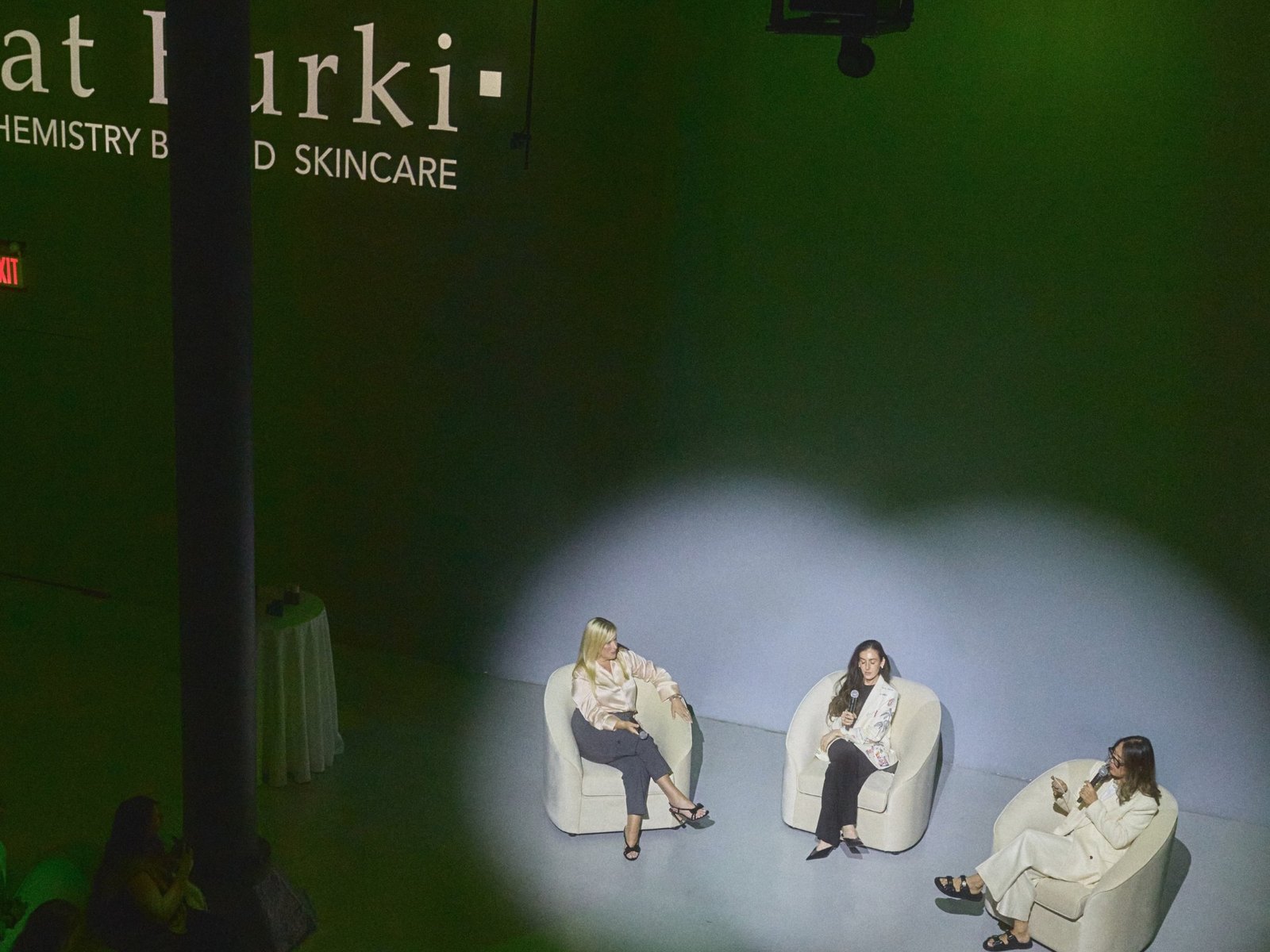 Panel discussion under a spotlight with the Kat Burki logo projected on the wall