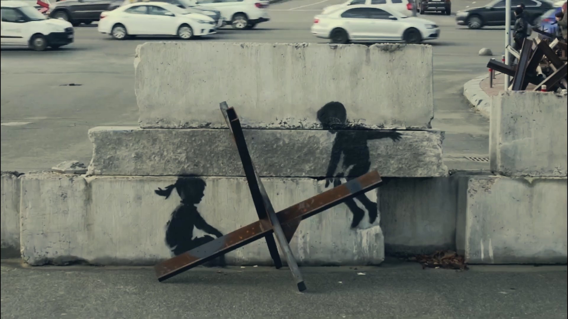Mural of two children on concrete blocks and an anti-tank hedgehog in Kyiv