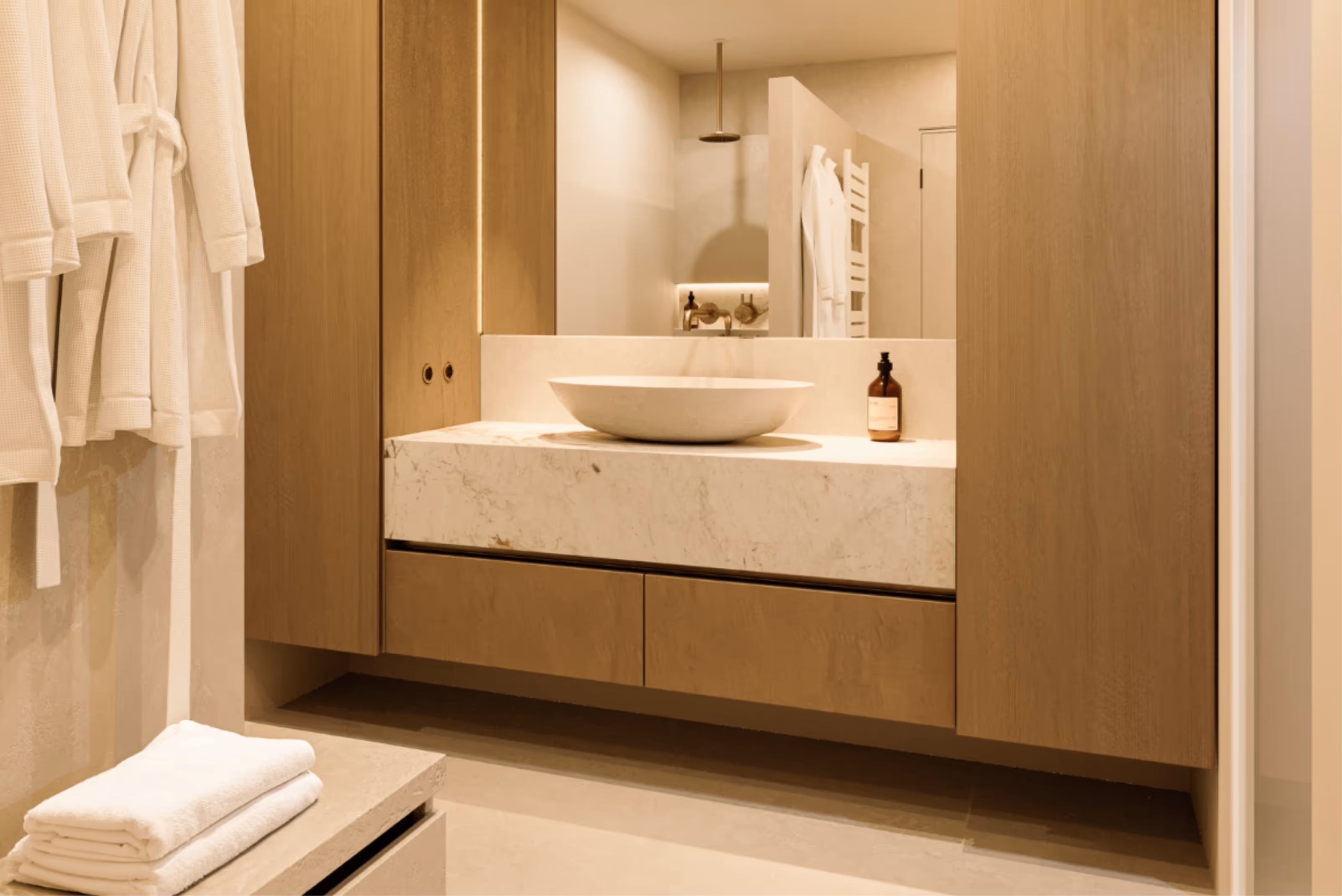 Moderne badkamer met marmeren wastafel, houten kasten en witte badjassen aan de muur.