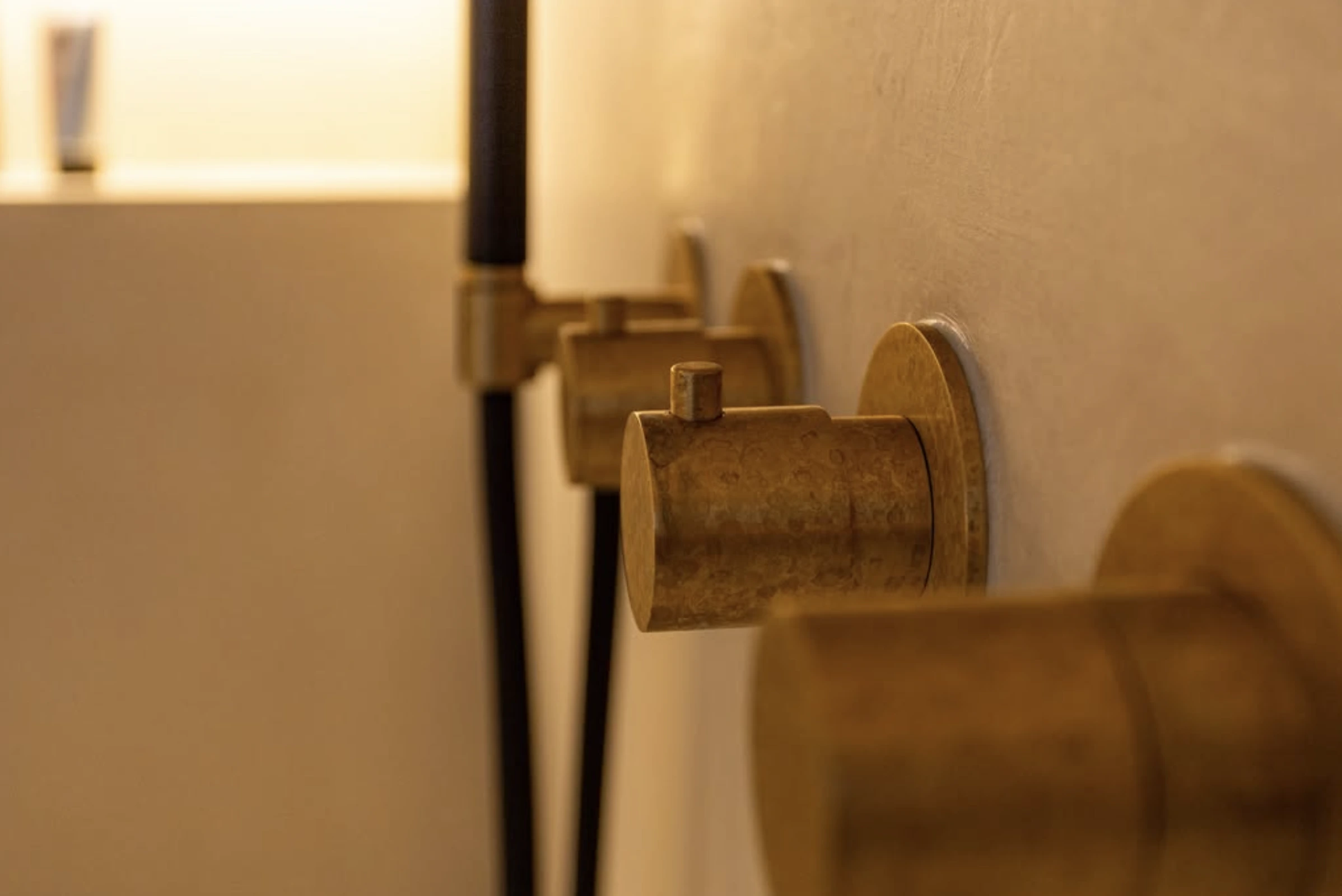Gouden doucheknoppen naast een wand met een zwarte douchekop op de achtergrond.