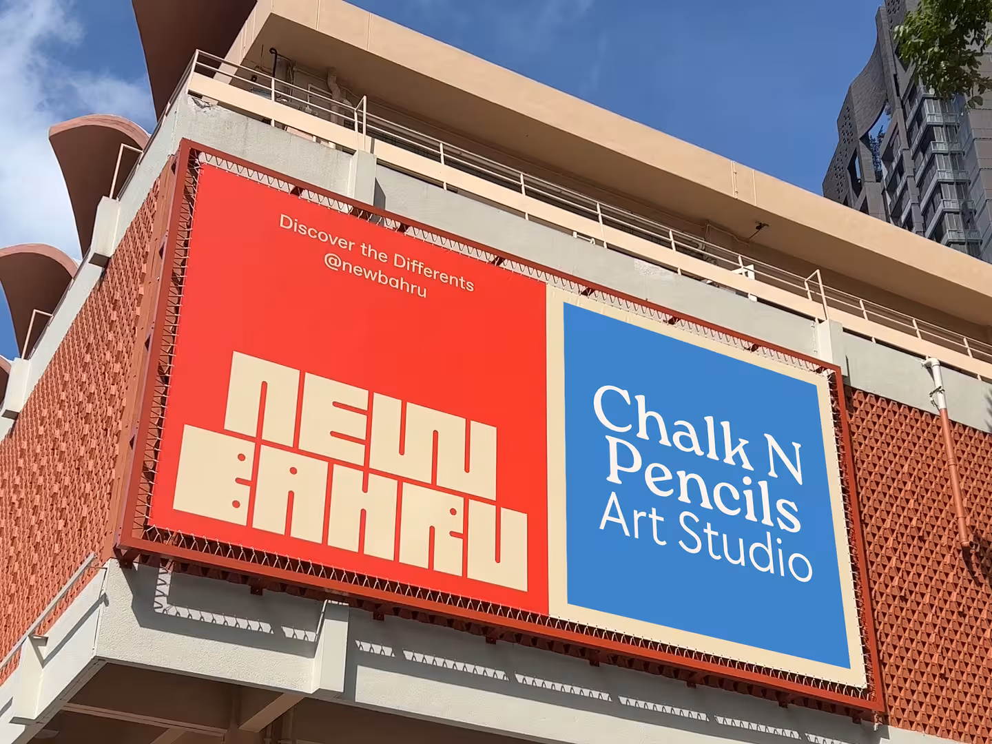 Outdoor billboard with red and blue panels; left panel reads 'NEW BAHRU' and right panel reads 'Chalk N Pencils Art Studio'.