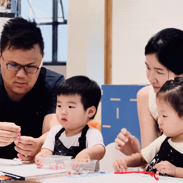 Two young children sitting at a table with two adults helping them with arts and crafts activities.