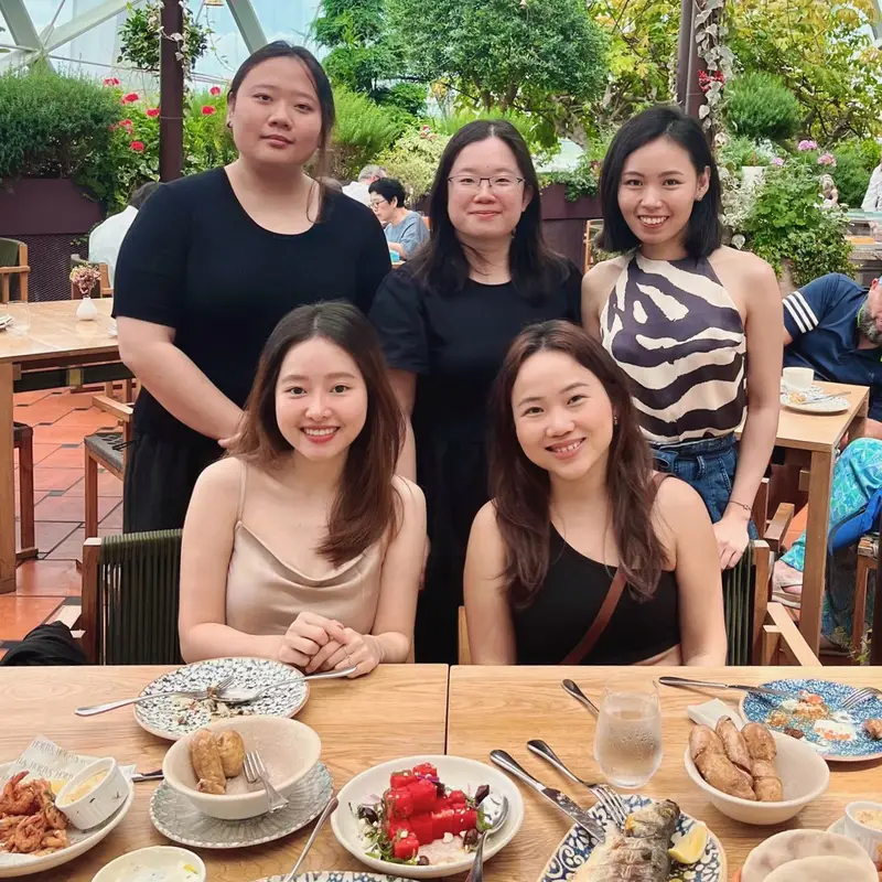 Group of five women smiling at a restaurant table with plates of food and drinks.