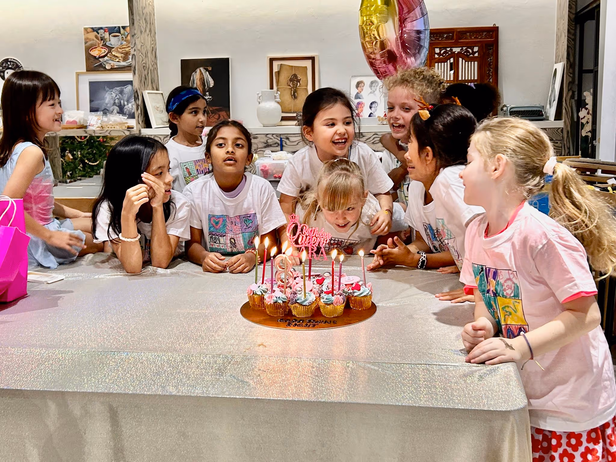 Group of children gathered around a birthday cake with lit candles, preparing to blow them out at a party.