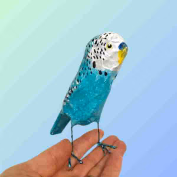 Hand holding a small blue and white bird sculpture with black spots and yellow markings on its face.