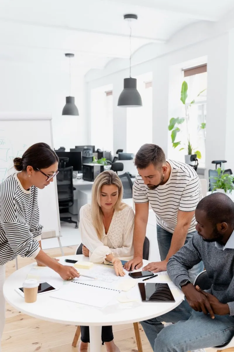 Four colleagues discussing work around a white table in a modern office.