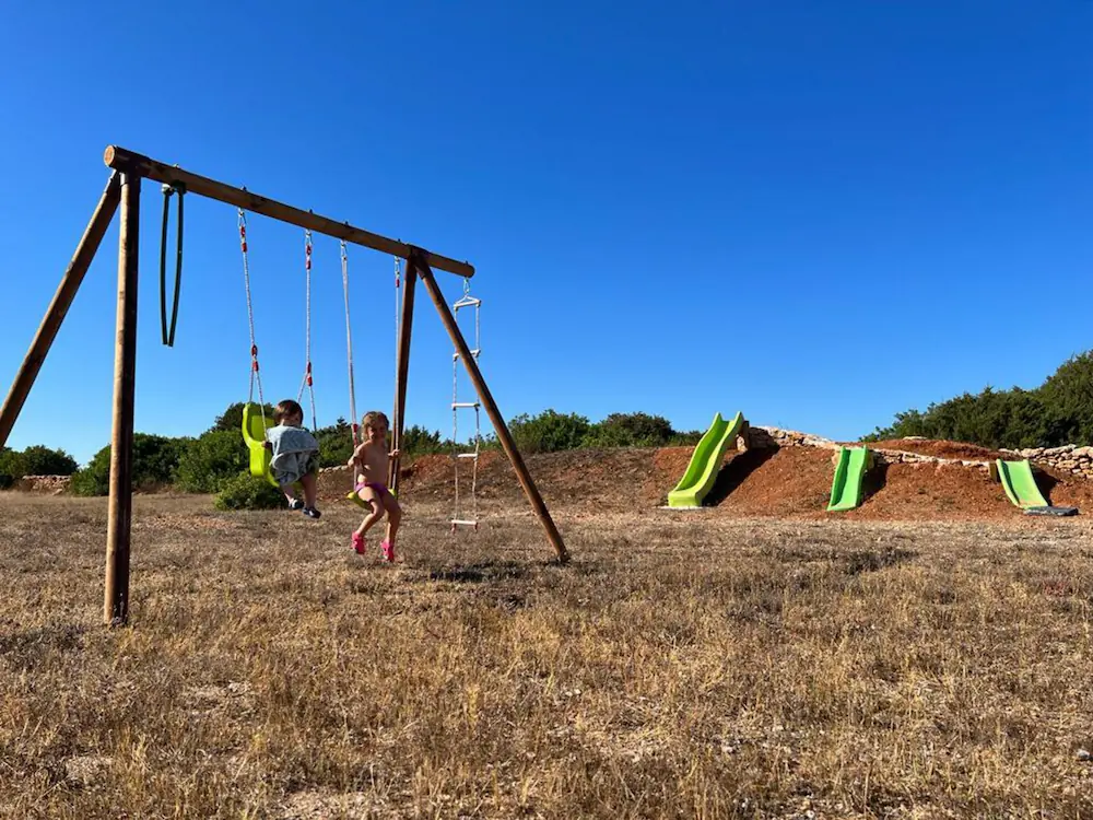 Zona de juegos infantil privada con columpios y toboganes en el terreno natural de la casa.