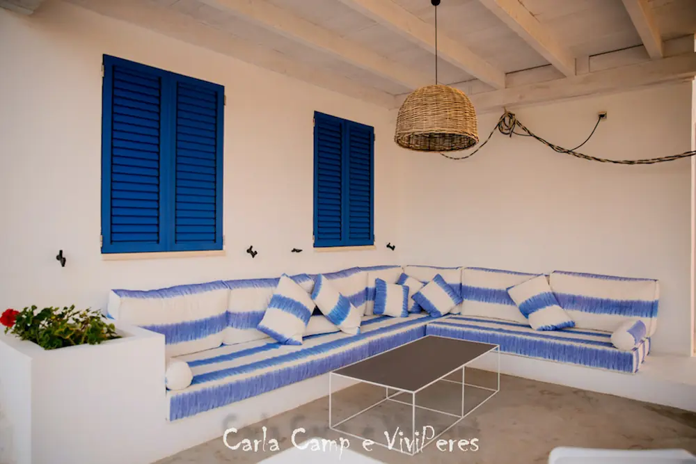 Rincón de relax en el porche exterior con sofá de obra blanco, cojines cómodos y mesa auxiliar rústica.