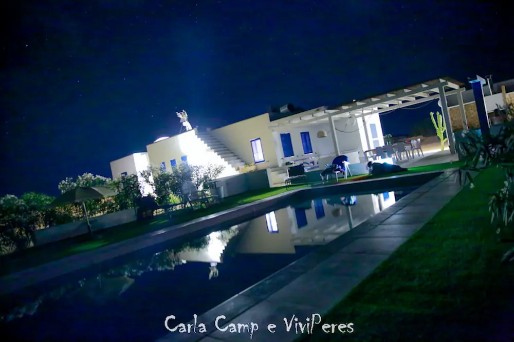 Iluminación nocturna de la piscina y fachada de la villa creando un ambiente exclusivo y relajante.