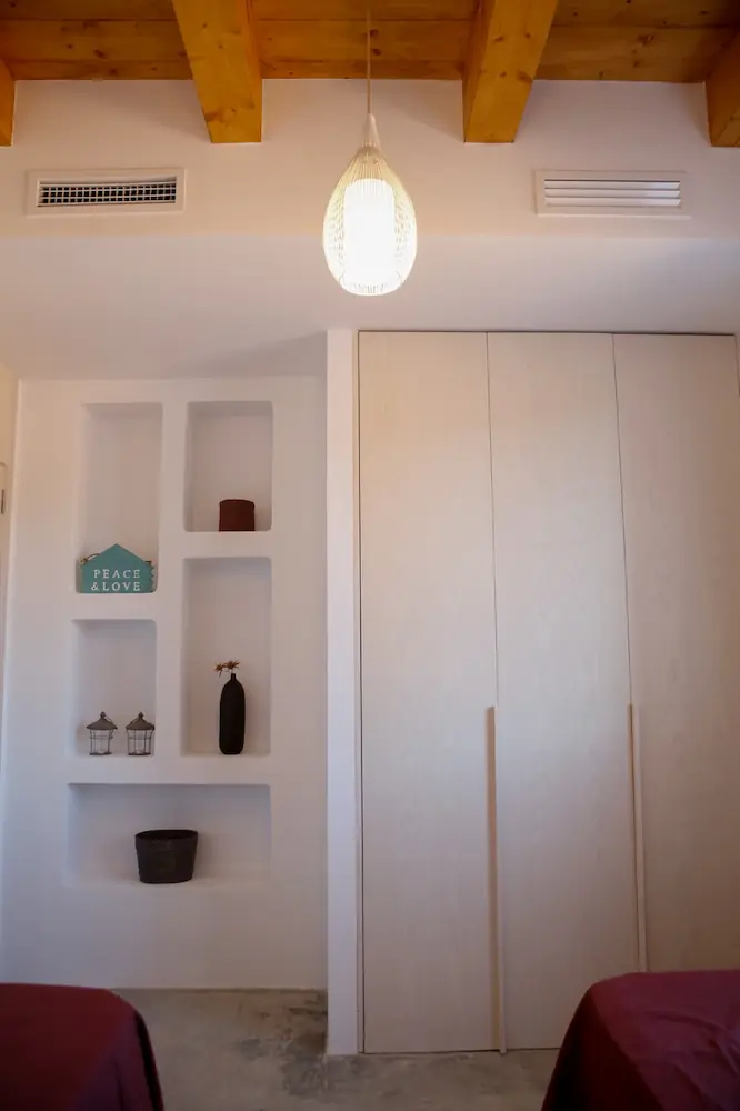 Habitación con armario blanco, estantes empotrados con decoración y techo con vigas de madera y lámpara colgante.