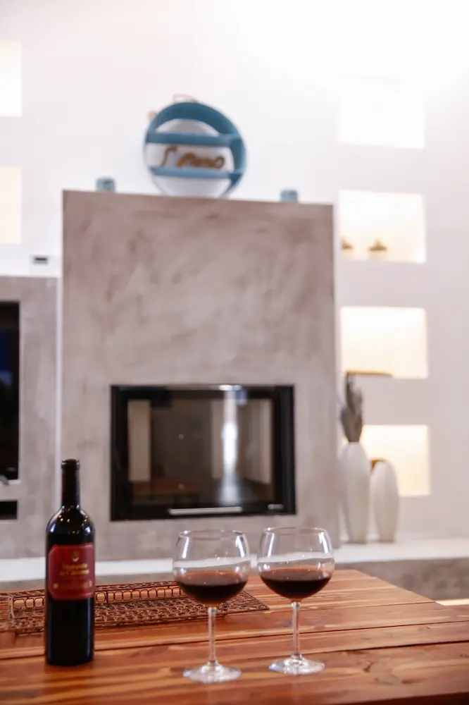 Botella de vino tinto y dos copas con vino sobre una mesa de madera frente a una chimenea moderna en un alojamiento en Formentera