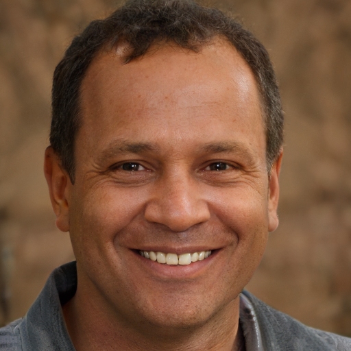Smiling middle-aged man with short curly hair wearing a gray jacket.