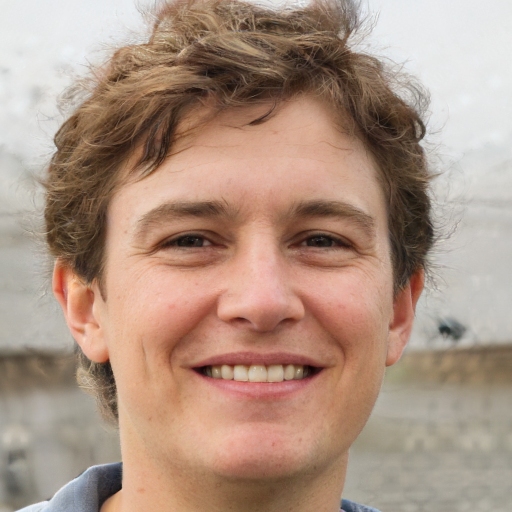 Smiling young man with curly brown hair wearing a blue collared shirt.