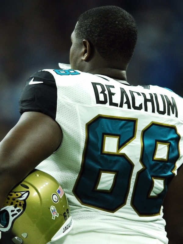 Kelvin wearing a white Jacksonville Jaguars jersey with the name Beachum and number 68, holding a gold helmet with the Jaguars logo.
