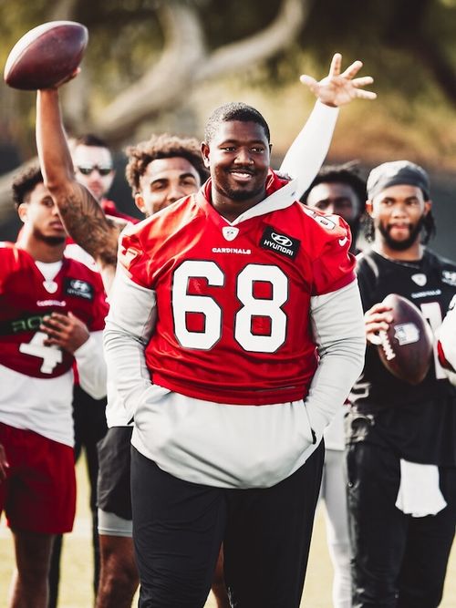 Smiling Kelvin wearing red number 68 Cardinals jersey with teammates in the background.