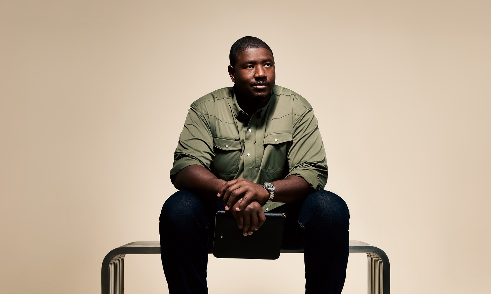 Kelvin in a green shirt and dark pants sitting on a modern bench, holding a black tablet.