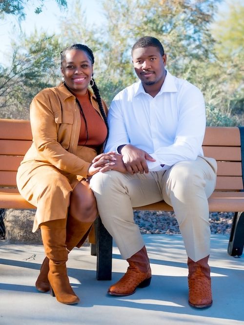 Kelvin and Jessica sitting closely on a bench outdoors with greenery in the background.