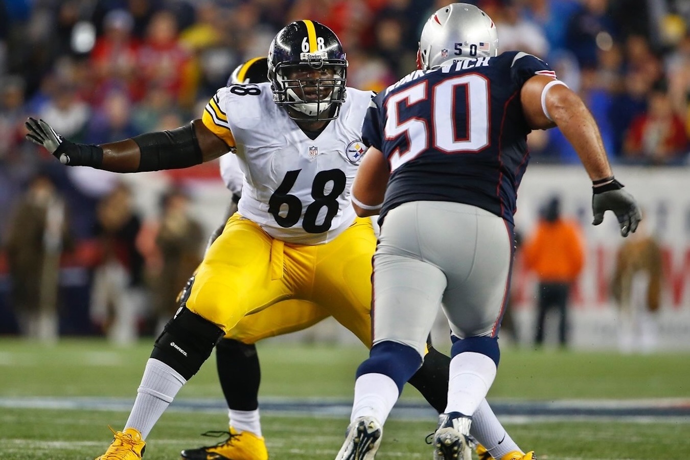 Kelvin as a Pittsburgh Steelers player wearing number 68 in white and yellow jersey facing New England Patriots player wearing number 50 in navy and gray jersey on a football field.