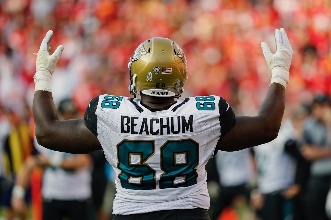 Football player Beachum, number 68, in Jaguars uniform raising both arms on the field.