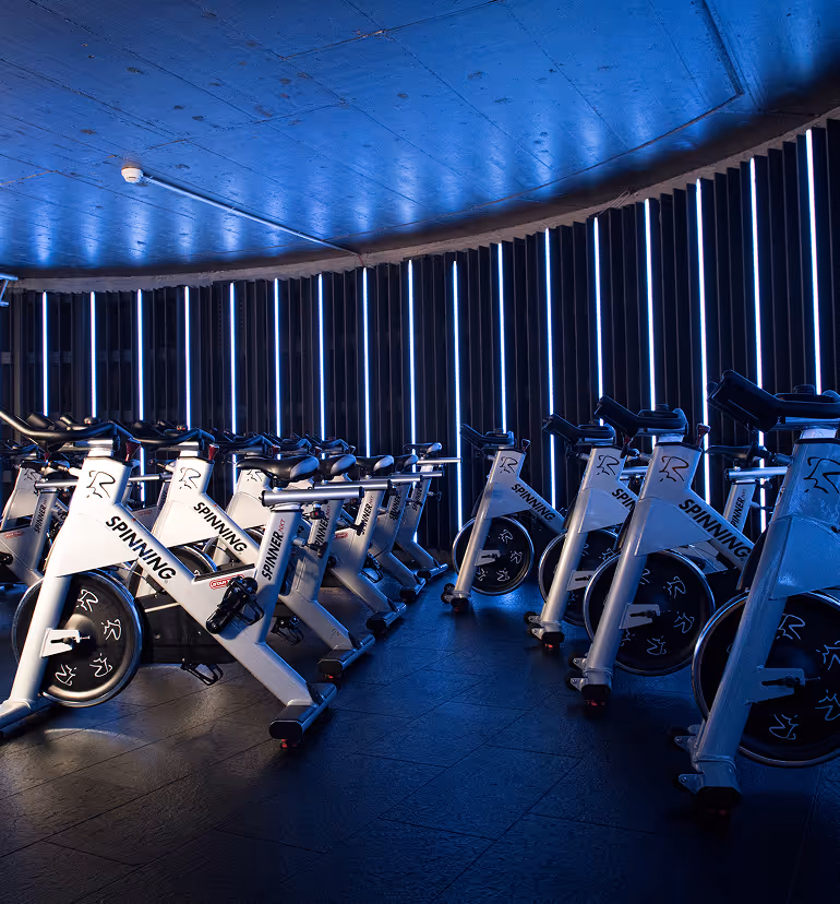 Indoor-Cycling-Geräte von Holmes Place mit blauer Umgebungsbeleuchtung für intensive Spinning-Workouts.