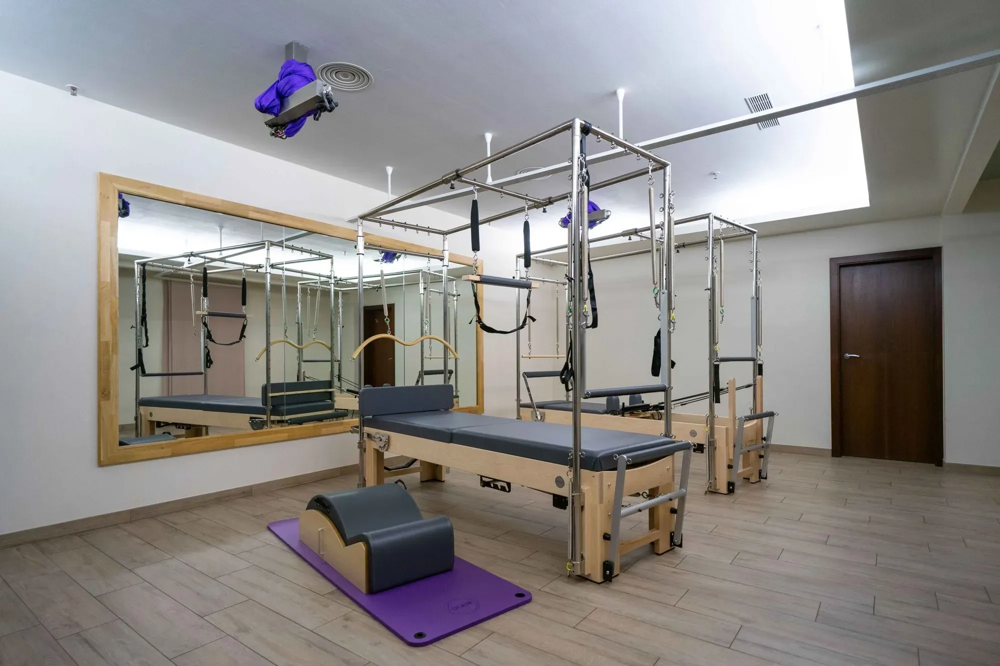 Das Pilates-Reformer-Gerät von Holmes Place verfügt über einen Spiegel, einen Holzboden und graue Trainingsmatten.