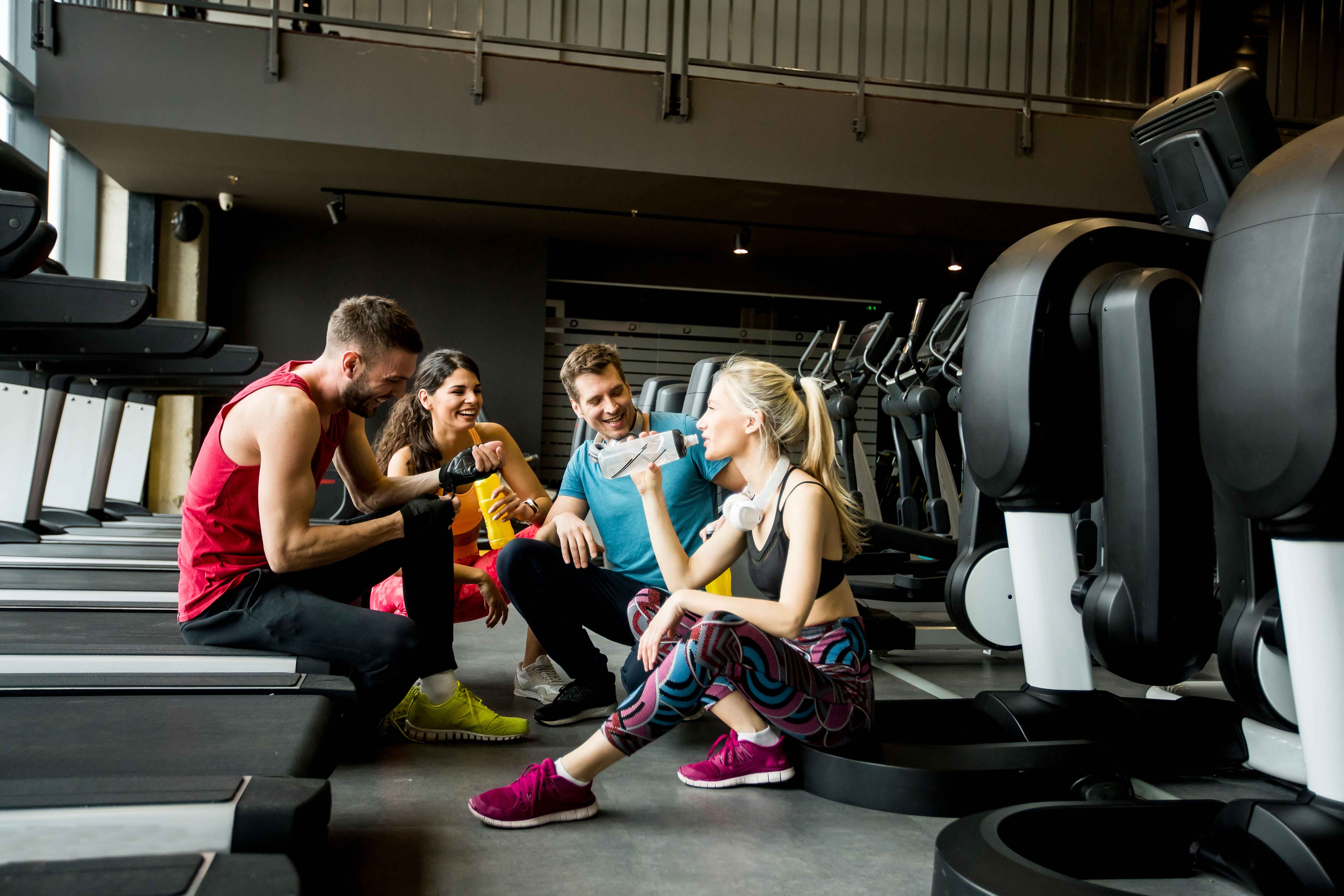 Menschen unterhalten sich und trinken im Fitnessstudio von Holmes Place inmitten von Trainingsgeräten und Laufbändern für ihre Fitness.