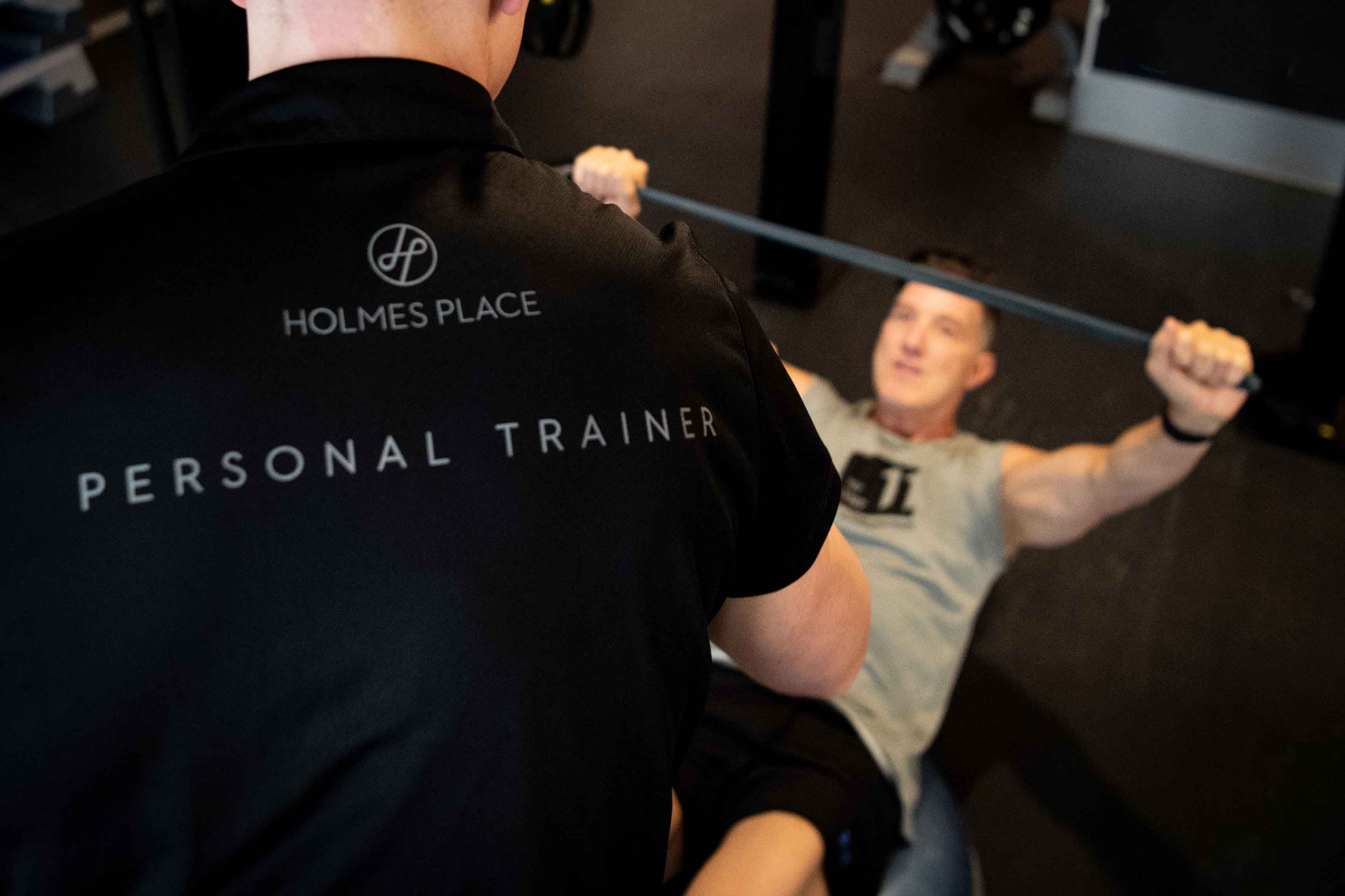 Der Personal Trainer von Holmes Place hilft seinen Kunden unter fachkundiger Anleitung beim Gewichtheben in einer sicheren Fitnessstudioumgebung