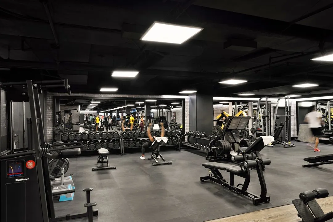 Innenraum des Fitnessstudios von Holmes Place mit Trainingsgeräten und Menschen, die trainieren und Fitnessübungen machen.