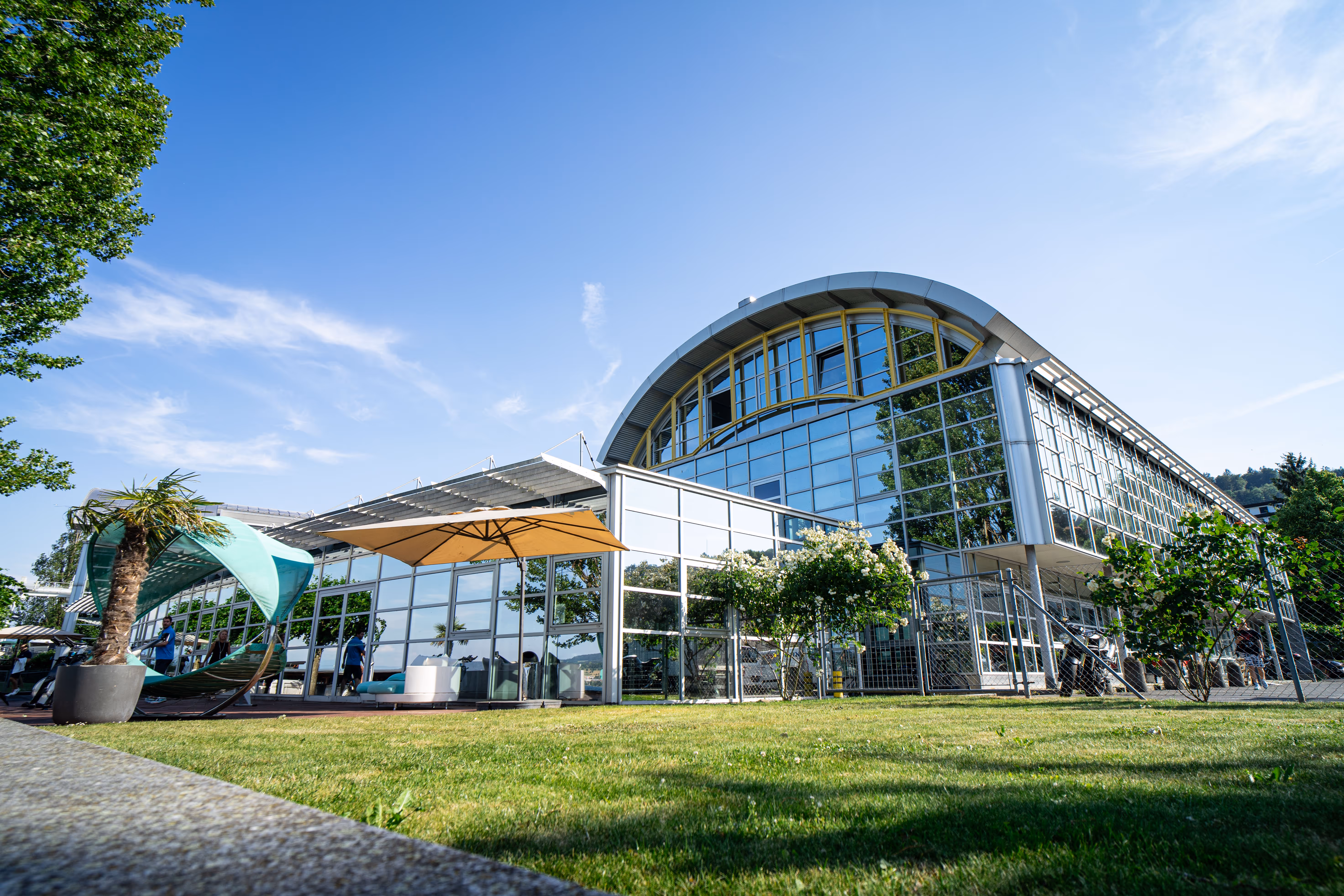 Außenbereich des Holmes Place Fitnesscenters mit Glasfassade und sonnigem Sitzbereich im Freien.
