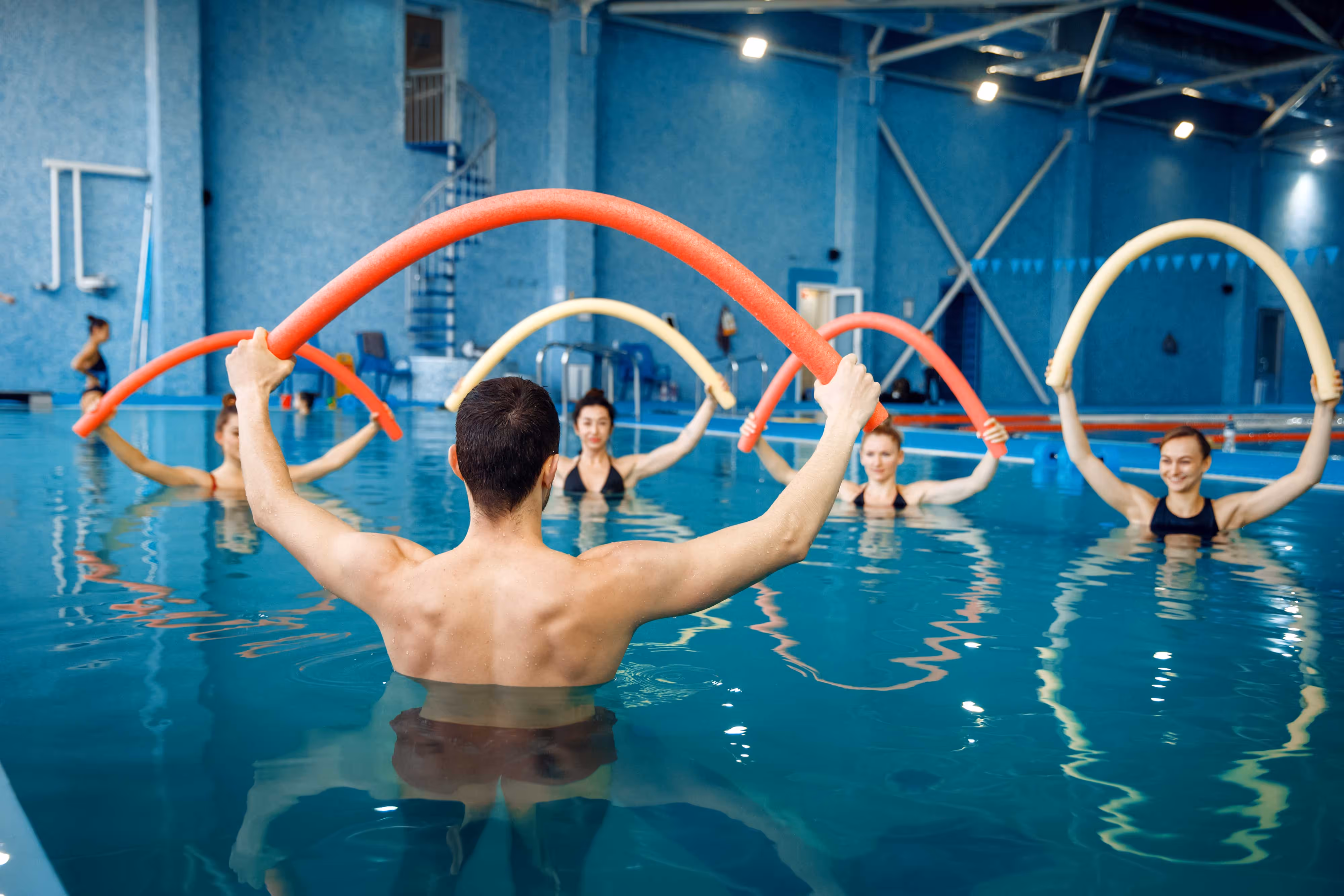 Mitglieder nehmen an einem Wassergymnastikkurs von Holmes Place mit Schaumnudeln in einem Pool teil.