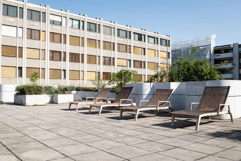 Moderne Loungesessel auf dem Dach von Holmes Place mit eleganten weißen Pflanzgefäßen und modernem Architekturhintergrund.
