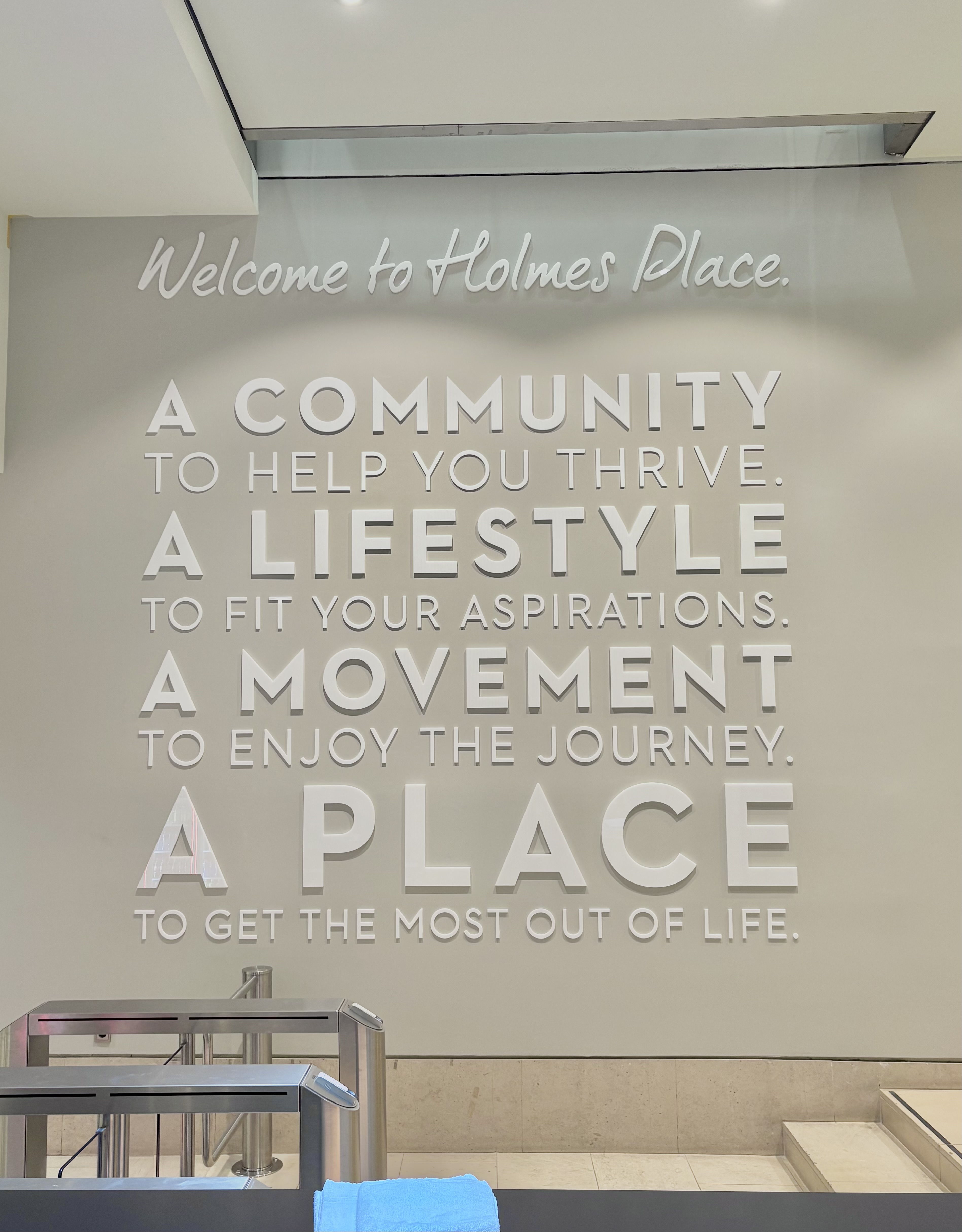 Der Eingang zum Fitnessstudio von Holmes Place ist mit einem motivierenden Zitat und einem Drehkreuz versehen.